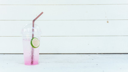 Fresh pink lemonade with lemon in plastic glass on white wooden