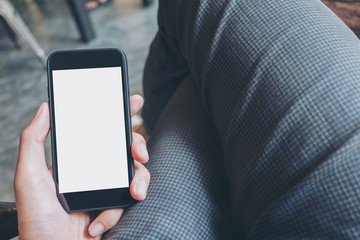 Mockup image of hand holding black mobile phone with blank white screen on thigh in modern cafe
