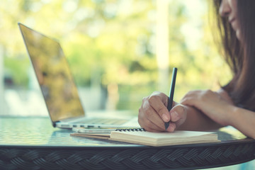 Fototapeta premium A woman writing on notebook and looking at laptop by outdoor swimming pool 