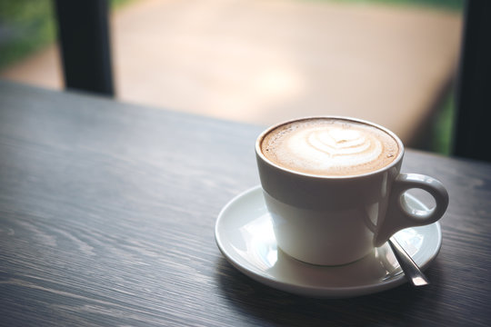 Closeup image of hot Latte coffee cup on vintage wooden table in cafe