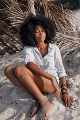 Obraz premium beautiful young african american girl sitting on sand at the beach