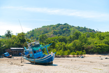 old fishing boat in blue standing on the rocks at low tide. Fishing village in Thailand.
