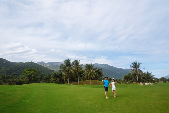 Young beautiful couple in love holding handsand walking at golf course in summer. man wear the blue shirt and the girl in a white dress. Concept of honeymoon