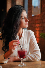 Girl drinks mulled wine in coffee shop.Lovely girl looking out the window in the restaurant and waiting for their friends. Young woman on a date in the cafe. Sexy girl in dreams is sitting in the cafe