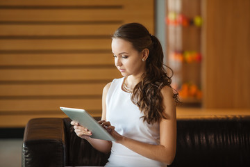 Pretty girl sitting on leather sofa and holding tablet