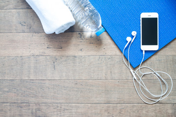 Flat lay of mobile phone with earphone and yoga mat, towel and b