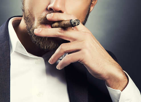 Cigar in hand of men wearing suit and white shirt. Toned skin studio shot over dark background