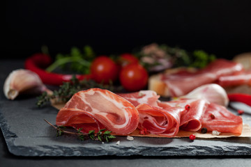 Ham , cherry tomatoes, red pepper and herbs on black stone slate board.