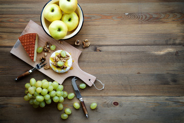Textured wood background with camembert and honey, walnuts, grapes, apples and goat cheese