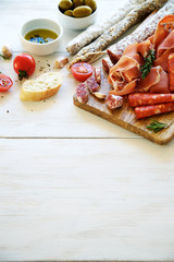 Antipasto with traditional Spanish meat snacks on wooden board and white wooden background 