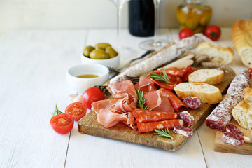 Antipasto with traditional Spanish meat snacks on wooden board and white wooden background 
