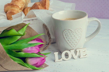 Cup of coffee with croissants, bouquet of pink tulips and wooden word LOVE