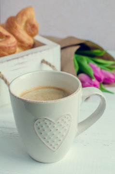 Cup of coffee with bouquet of pink tulips and croissants