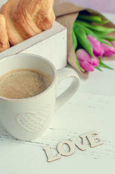 Cup of coffee with croissants, bouquet of pink tulips and wooden word LOVE