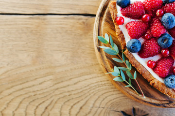 A piece of berry tart with raspberries and blueberries on wooden background with copy space © igishevamaria