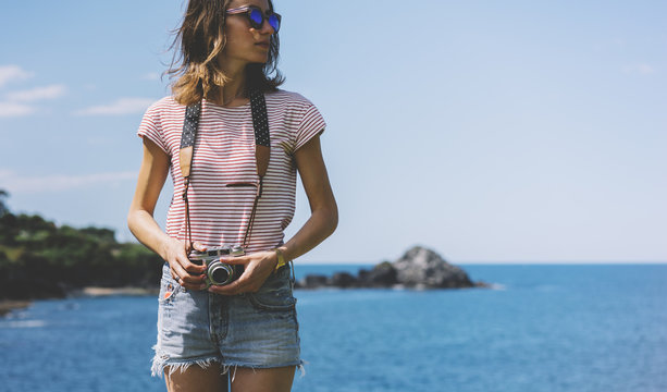 Tourist traveler photographer making pictures seascape on vintage photo camera on background piar, hipster girl enjoying peak mountain and nature holiday, mockup ocean waves view, blurred backdrop