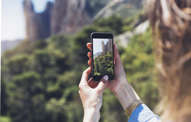 Hipster girl making photo on smartphone mobile, view tourist hands using gadget phone in travel on background mountains and sky landscape; finger touch screen cellphone mockup nature, templates