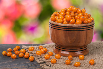 Sea-buckthorn berries in a wooden bowl on table with blurred garden background