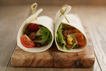 tortilla wrap sandwiches with beef and vegetables on olive board, closeup photo with shallow focus