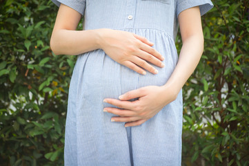 Close up of pregnant woman are relaxing in the garden at house. pregnant woman holding her belly in the garden
