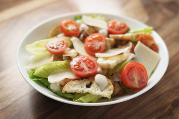 fresh caesar salad with chicken and cherry tomatoes on wood table, shallow depth of field