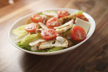 fresh caesar salad with chicken and cherry tomatoes on wood table, shallow depth of field