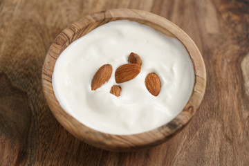 homemade yogurt with almonds in wood bowl on wooden table, shallow focus