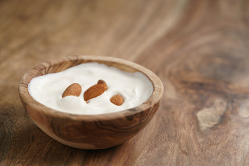 homemade yogurt with almonds in wood bowl on wooden table, shallow focus