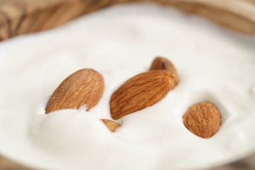 macro shot of homemade yogurt with almonds in wood bowl on wooden table, shallow focus