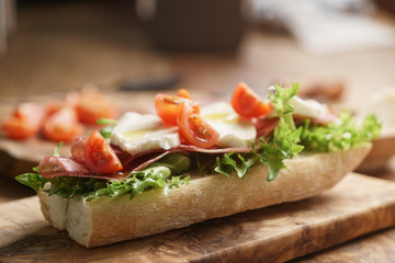 open sandwich with prosciutto, mozzarella and tomatoes on kitchen table, shallow focus