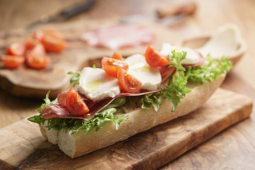 open sandwich with prosciutto, mozzarella and tomatoes on kitchen table, shallow focus