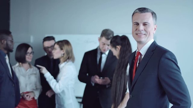 Joyful adult man looking back to colleagues and looking at camera.