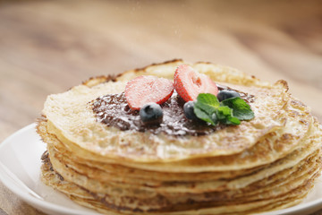 fresh blinis or crepes with melted dark chocolate, berries and sugar powder, shallow focus