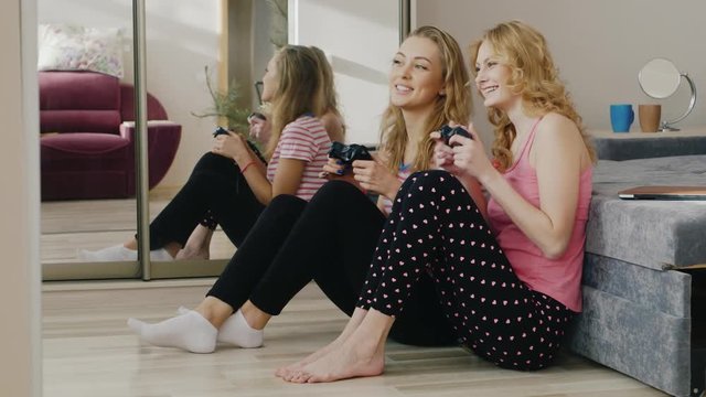 Two young women playing on the console. Sit on the floor near a mole. Have fun together, girlfriends pajama party