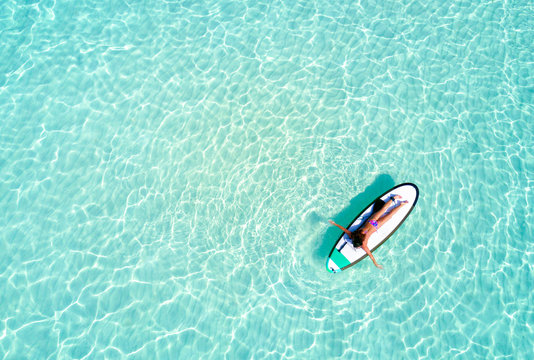 Frau auf Surfbrett paddelt &uuml;ber das t&uuml;rkise Wasser der Malediven