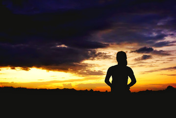 woman silhouette standing in front of a sun setting sky