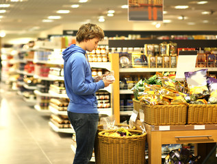 Man shopping in supermarket reading product information. Checking list.
