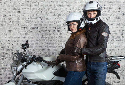 Young embracing couple in a motorcycle outfit standing together near the motorbike in the garage