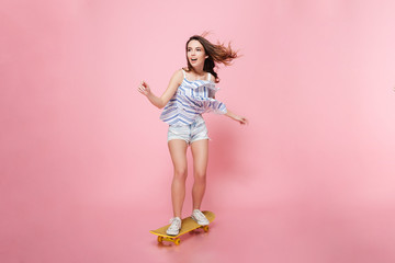 Full length of happy carefree young woman riding on skateboard