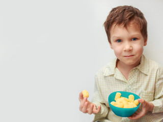 little smiling boy eating corn sticks on a background of space for text