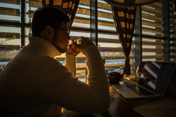 man in sweater working on laptop in caffe on sunset