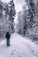 Vertical picture of a man standing on road covered with snow leading through the forest