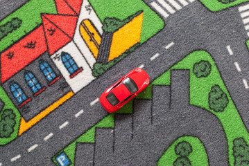 Red toy car on a city themed carpet, city street concept - Powered by Adobe