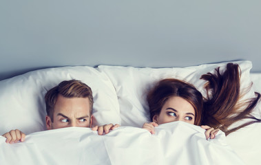 Playfull couple peeping from bedsheet