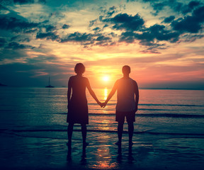 Silhouette of couple holding hands on the sea beach during sunset.