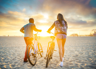 couple walking bikes together on beach to stunning sunset