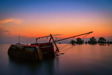 The old fishing boat capsized on sea at sunset in Phuket, Thailand