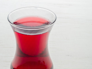 Hibiscus tea in a glass mug on a wooden table among rose petals and dry tea custard