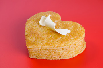 Pile of pancakes in the shape of a heart on red with curl of but