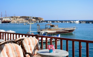 Tables and chairs at a waterfront bar with views across the harbour, Hersonissos, Crete.